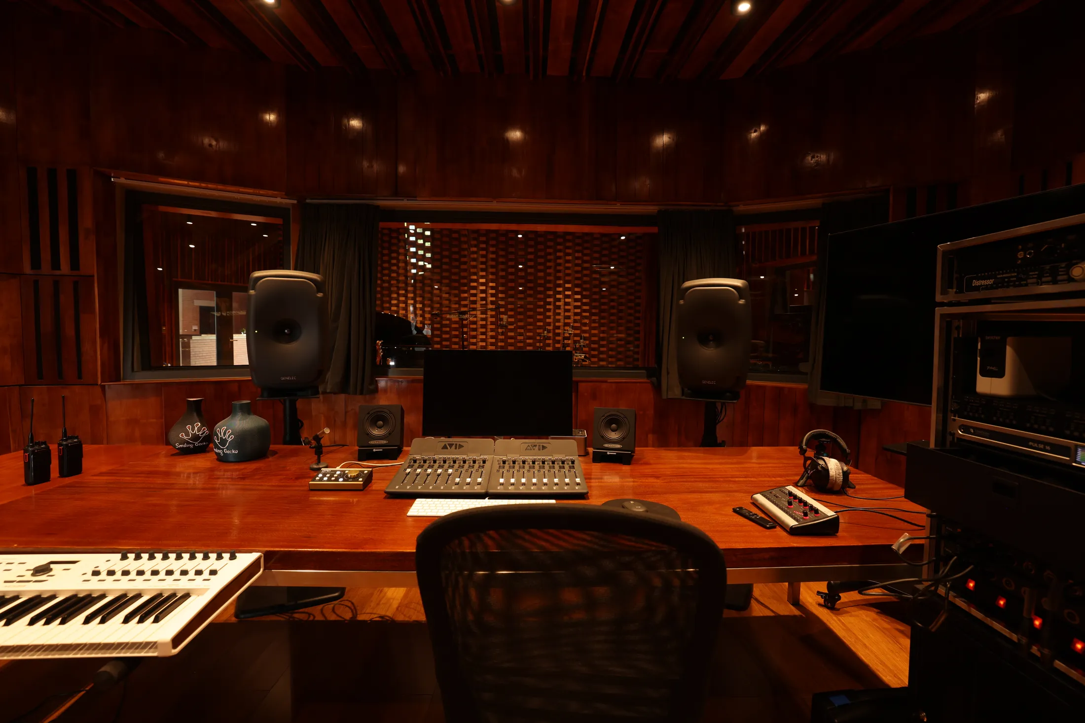 The control room — mixing console and reference monitors on a wooden desk, with the live room through the window