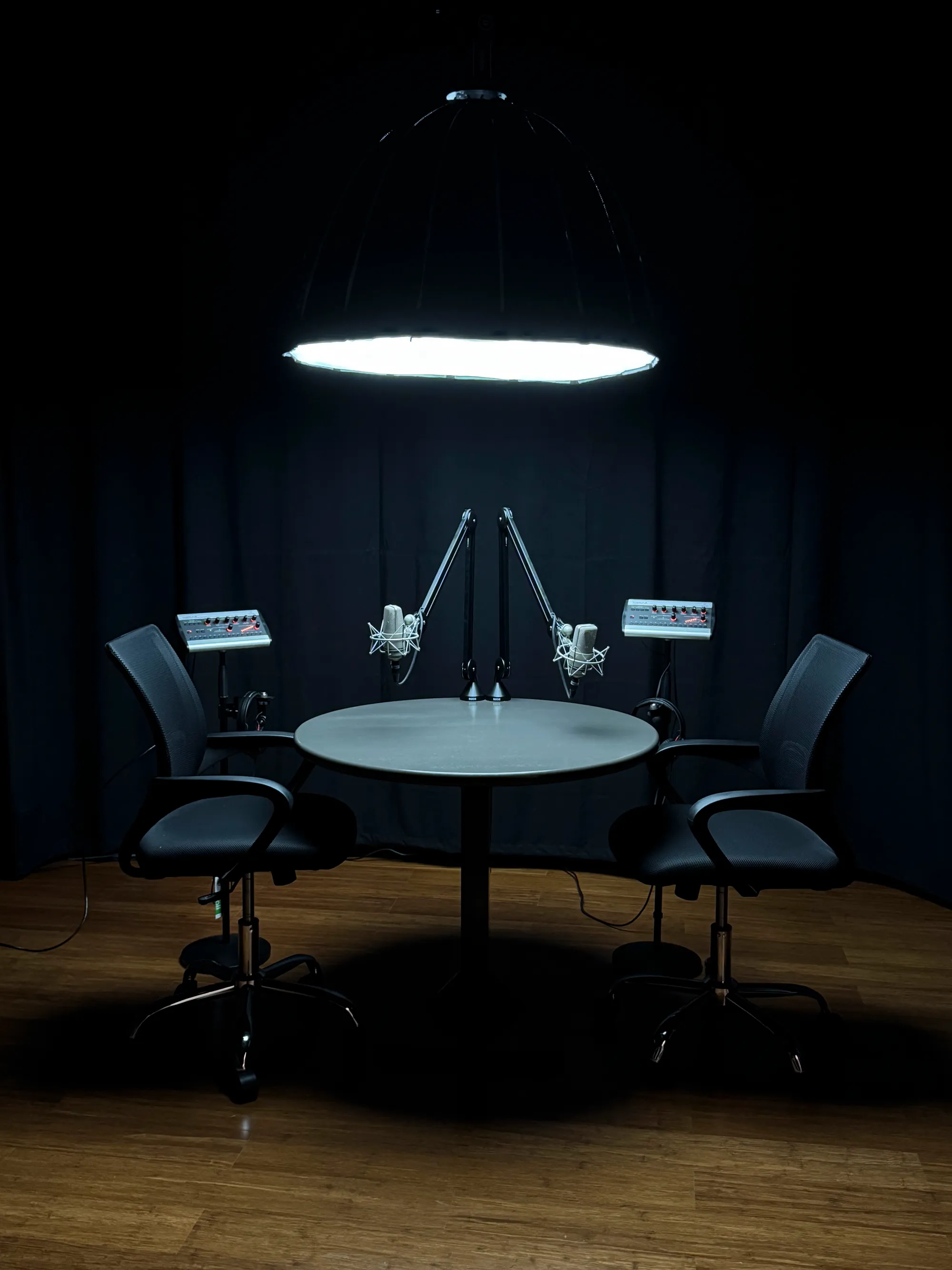 The podcast studio — two microphones face each other across a round table under a single hanging light